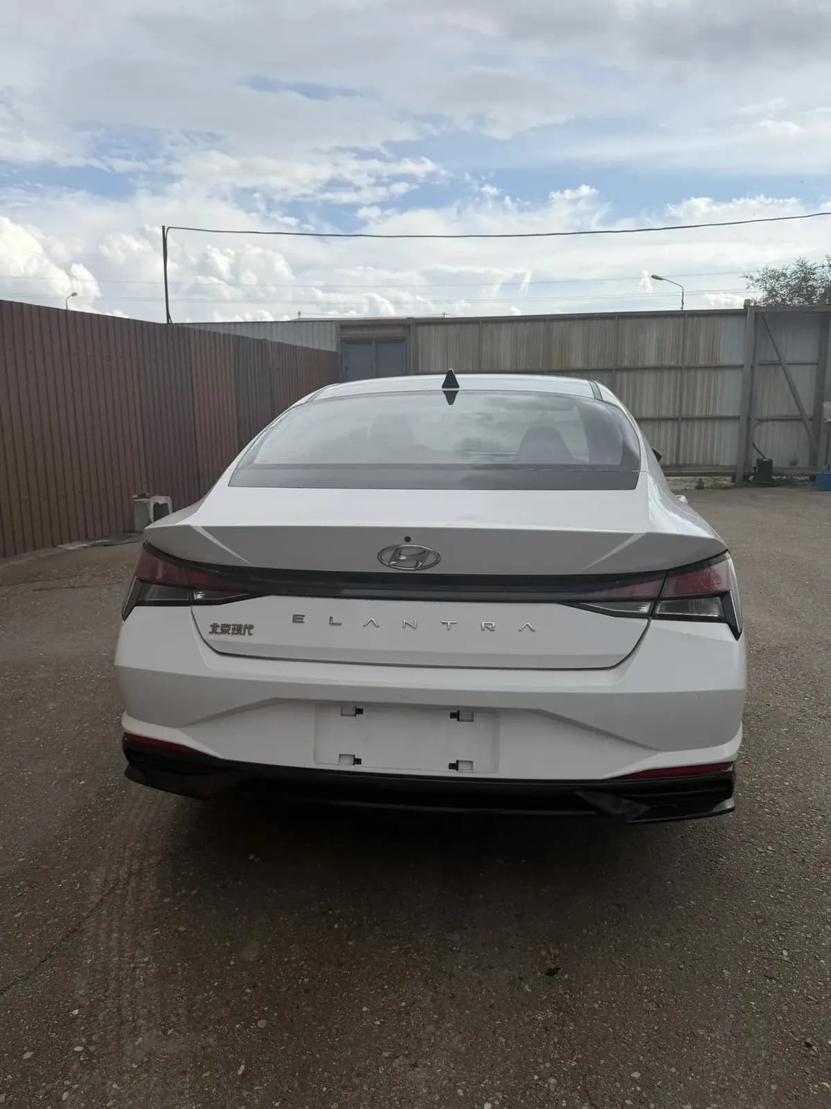 Белая Hyundai Elantra сзади: крышка багажника со шильдиком Elantra, за машиной забор