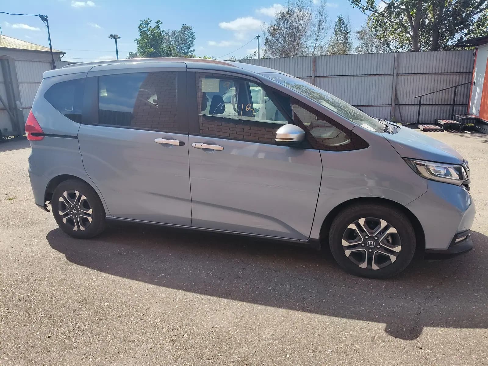 Honda Freed на площадке приёмки: правый борт, за машиной забор и деревья